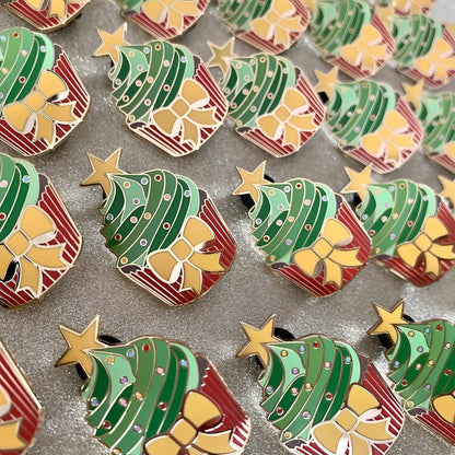 The image shows rows of many pins. The pins are in the shape of cupcakes with a yellow star at the top. Each cupcake has a red bottom, brown sponge, and the icing is different shades of green. There is a yellow bow on the red cup and there are multicoloured circles as sprinkles on the green enamel areas.