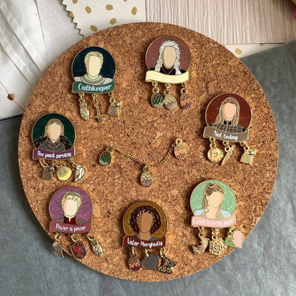 The picture shows all 7 Women of Westeros pins, each with three charms, a shimmery pearl swirl background, and the image of a character with a relevant quote in screenprint below.